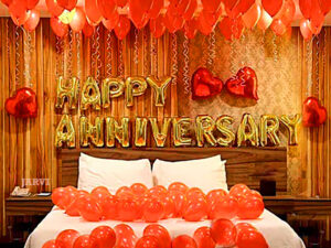 Marriage anniversary decoration with heart shaped foil and balloons on bed