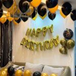 Simple birthday decoration with 2 heart/star-shaped foil balloons, 50 air-filled metallic balloons on ceiling with ribbon, and 10 metallic balloons spread on the floor and happy birthday foil balloon alphabet letter