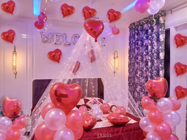 bed canopy decoration with balloons attached to ceiling with tape and hanging ribbons remaining as bunches on walls or loose on floor, fairy light, heart shaped red foil balloon, occasion foil (you choose from welcome, i love you, happy birthday or happy anniversary) and rose petals
