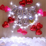 Wedding proposal decoration with heart shaped foil balloons, white balloons spread on the floor and led light string
