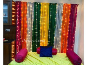 Simple Haldi/Mehandi decoration with backdrop of made of colorful mix clothes and 15-18 fairy light strings