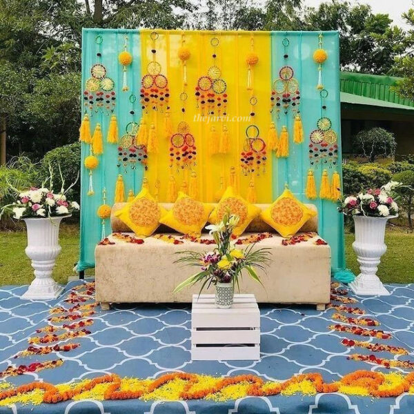haldi/mehendi decoration with yellow-blue curtain backdrop, flower petals and artificial fancy wall hangings on backdrop curtain